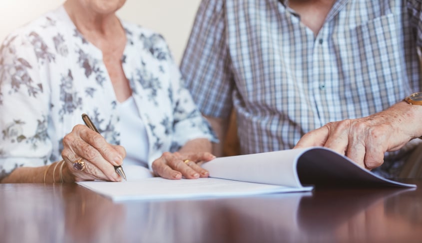 An elder couple signing paperwork symbolizing financial abuse.