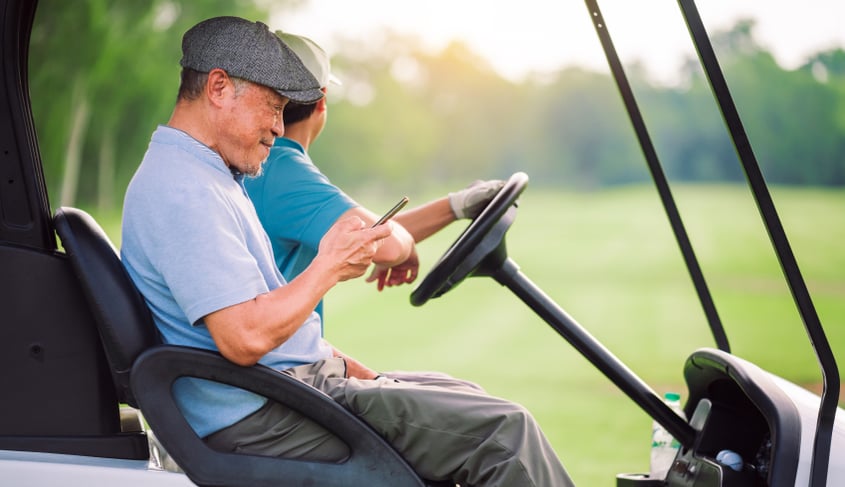 A man riding on a golf cart while looking at his phone, illustrating a person that may need a golf cart accident lawyer.